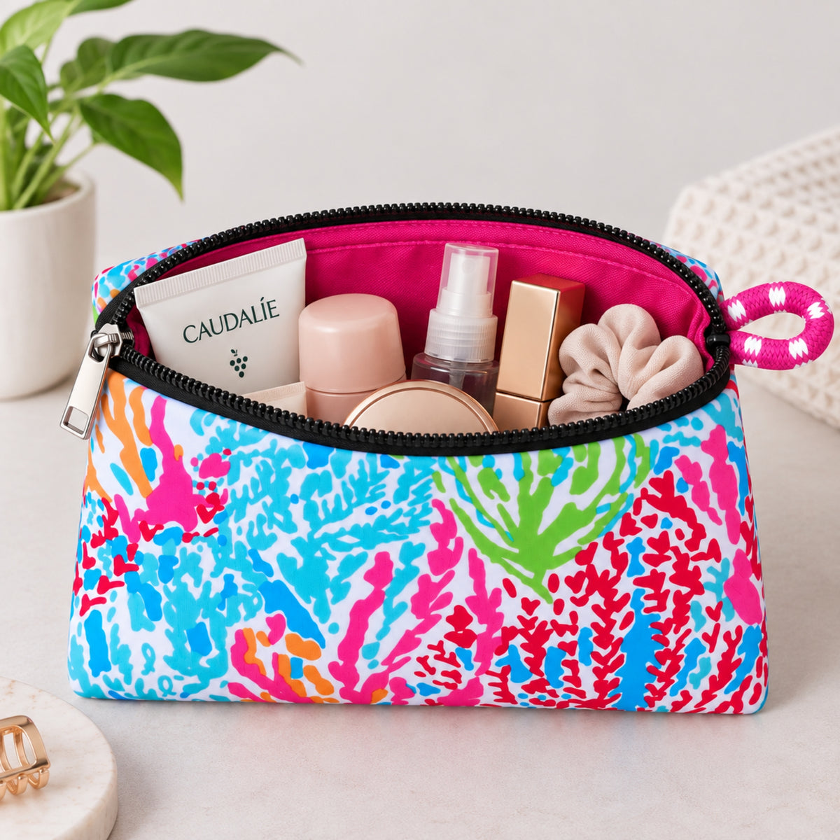 Neceser de neopreno Corales con estampado multicolor, cierre negro y productos de cuidado personal en su interior.
