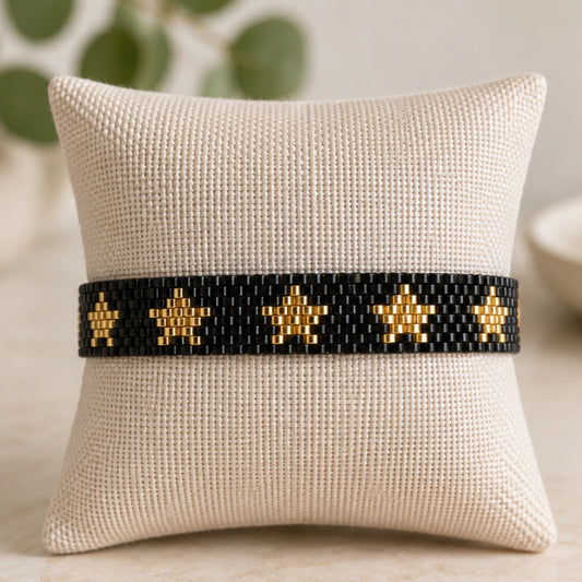 Pulsera de cuentas negra y dorada con diseño de estrellas.